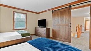 Une chambre avec deux lits, une commode, un téléviseur et une porte coulissante de style rustique.