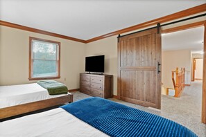 A bedroom with two beds, a dresser, a television, and a sliding barn-style door.