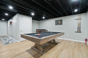 A pool table in a room with wooden flooring, a white door, and a ceiling with exposed beams.