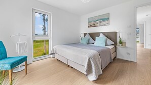 Una camera da letto con un'ampia finestra, un letto con molti cuscini, una sedia e un quadro appeso al muro.