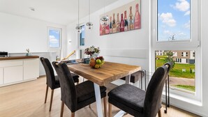 Una cucina moderna con un tavolo da pranzo in legno, sedie nere e una cesta di frutta. È presente un'ampia finestra con vista all'esterno.