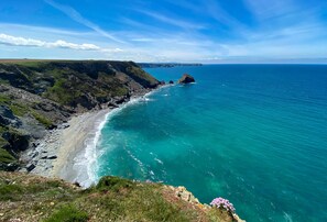 A coastal landscape with a rocky shoreline, clear blue sea, and distant landforms.