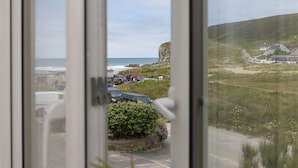 Vista costera a través de una ventana, con coches aparcados y una zona verde.