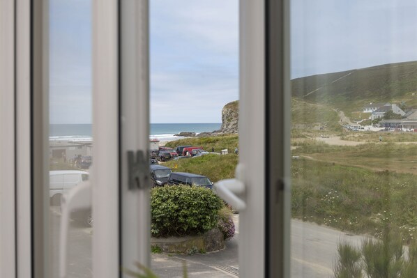 A coastal view through a window with parked cars and a grassy area.