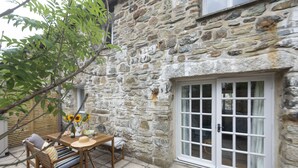 A stone building with a wooden table and chairs, a window, and a door with glass panels. - Sublimely located in the thriving village of St Agnes, just a stone's throw from the beauty of Cornw (St Agnes)