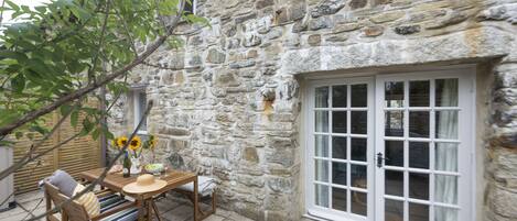 A stone building with a wooden table and chairs, a window, and a door with glass panels.