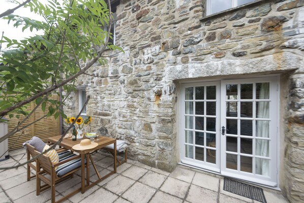 A stone building with a wooden table and chairs, a window, and a door with glass panels. - Sublimely located in the thriving village of St Agnes, just a stone's throw from the beauty of Cornw (St Agnes)