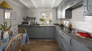 A modern kitchen with grey cabinets, a wooden dining table with chairs, a yellow pendant light, and a window with blinds. - Sublimely located in the thriving village of St Agnes, just a stone's throw from the beauty of Cornw (St Agnes)