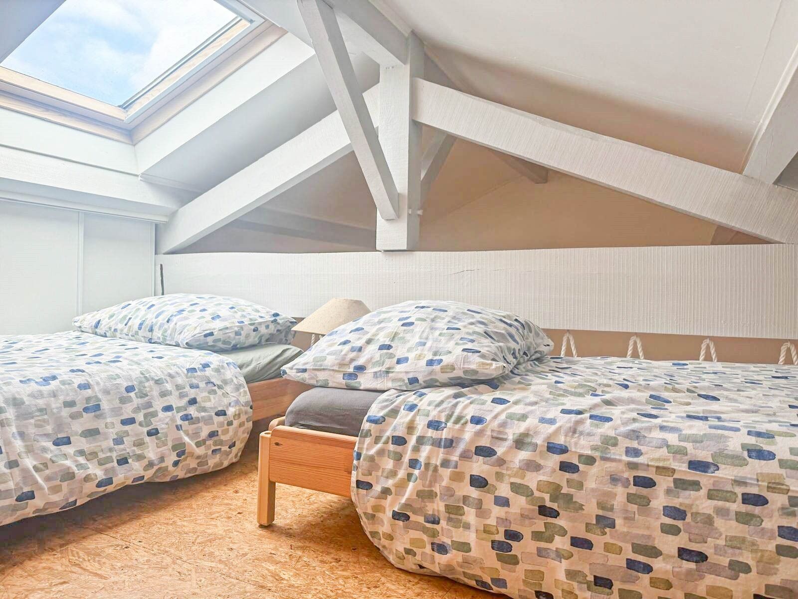 Une chambre avec deux lits, une lucarne et un plafond en pente.