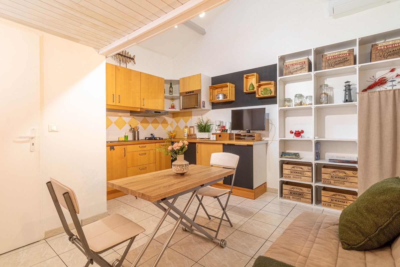 A compact kitchen with wooden cabinets, a dining table with chairs, a microwave, and a television.