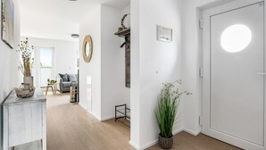 Un intérieur moderne avec un plancher en bois, une porte blanche et un couloir menant à un espace de vie comprenant un canapé et une table à manger.