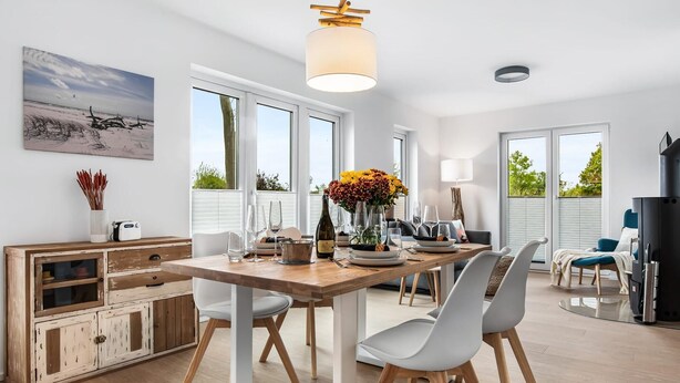 Une cuisine moderne avec une table en bois dressée pour le repas, de grandes fenêtres et une vue sur l’extérieur.