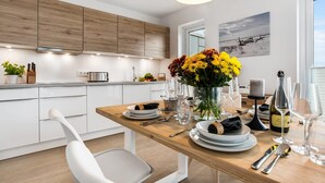 Une cuisine moderne avec des meubles blancs, une table à manger en bois mise pour le repas et un vase rempli de fleurs jaunes.