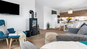 Un salon moderne doté d’un poêle à bois noir, d’un téléviseur à écran plat et d’un coin repas avec une table et des chaises en bois.