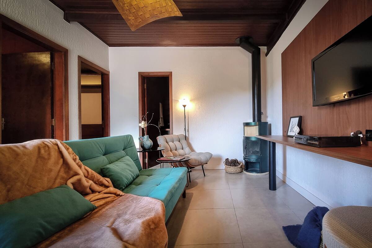 Un soggiorno con un divano verde, una poltrona beige, una televisione montata su una parete in legno e un camino.