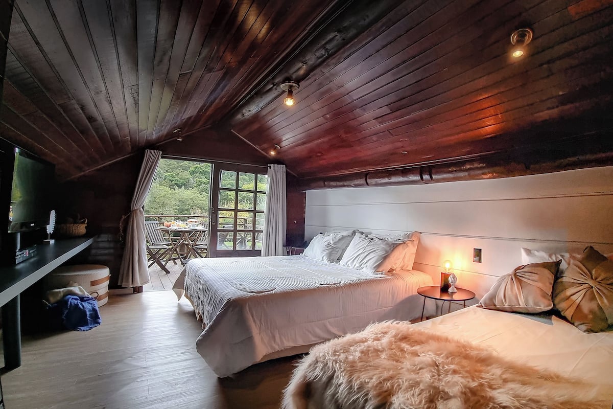 Una stanza accogliente con soffitto in legno, un letto con biancheria bianca, un tavolino con una lampada e un televisore su un mobile.