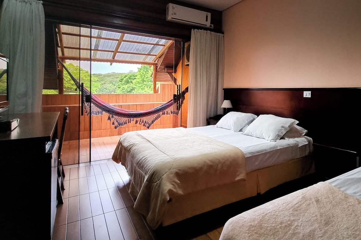 Camera d'albergo con due letti, un'amaca, una scrivania e vista sul verde.