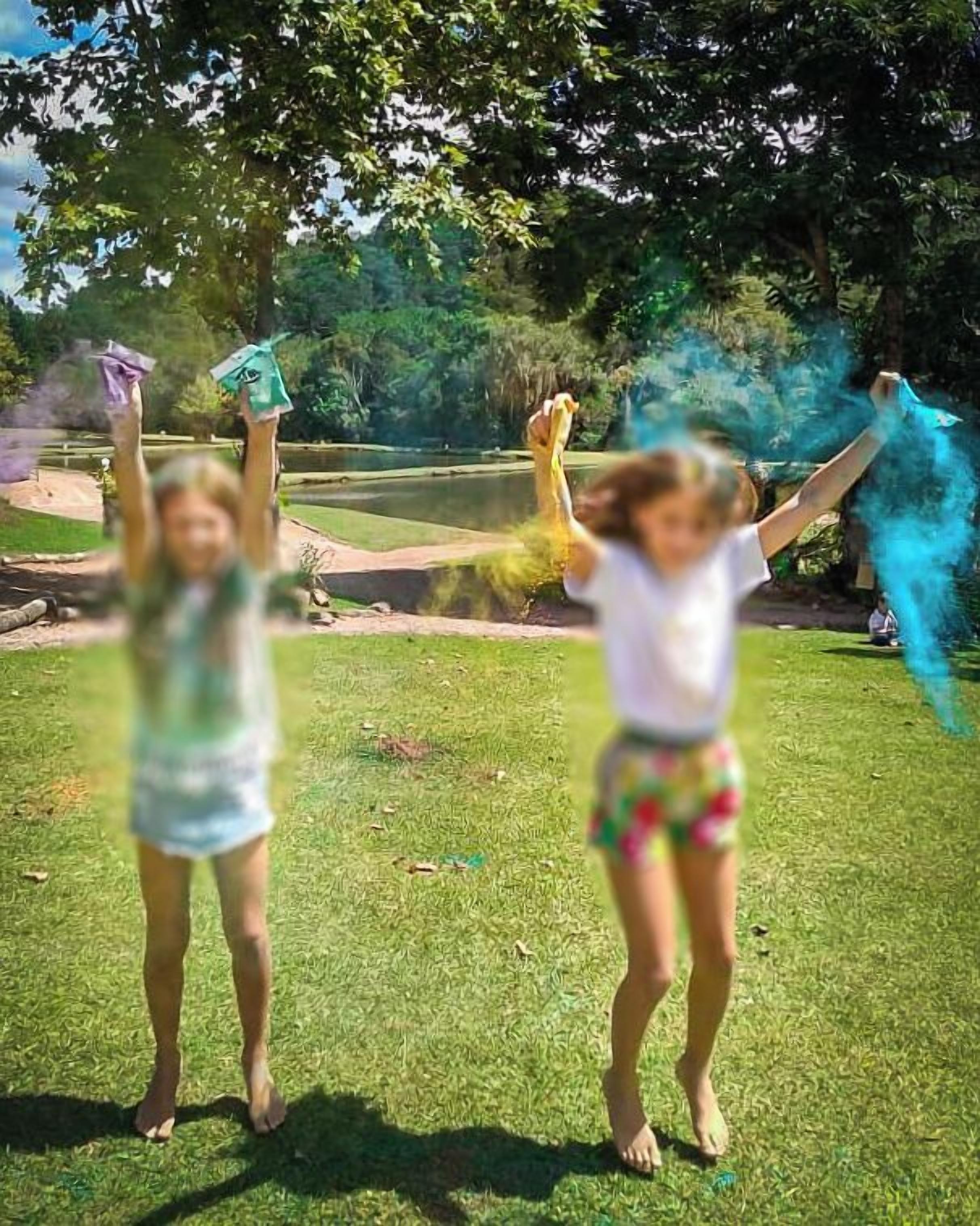 Dos niños jugando en un área verde con árboles al fondo.