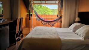 Hotelkamer met een bed, een bureau met een televisie, een hangmat en uitzicht op groen.