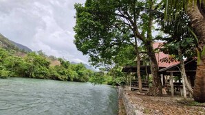 A river with lush greenery and a wooden structure with a red roof. - Yaxlik River lodge (San Agustin Lanquin)