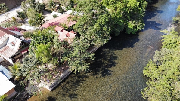 An aerial view of a riverside property with a dock, lush greenery, and a clear river. - Yaxlik River lodge (San Agustin Lanquin)