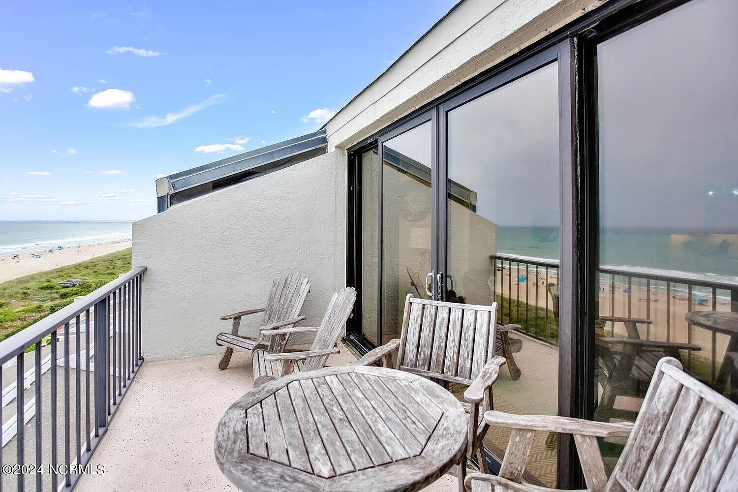 Ein Balkon mit Blick auf den Strand, ausgestattet mit Holzstühlen und einem Tisch.