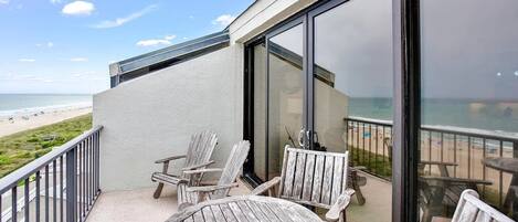 Ein Balkon mit Blick auf den Strand, ausgestattet mit Holzstühlen und einem Tisch.