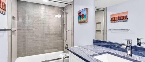 A modern bathroom with a glass-enclosed shower, a white toilet, and a marble countertop with a sink.