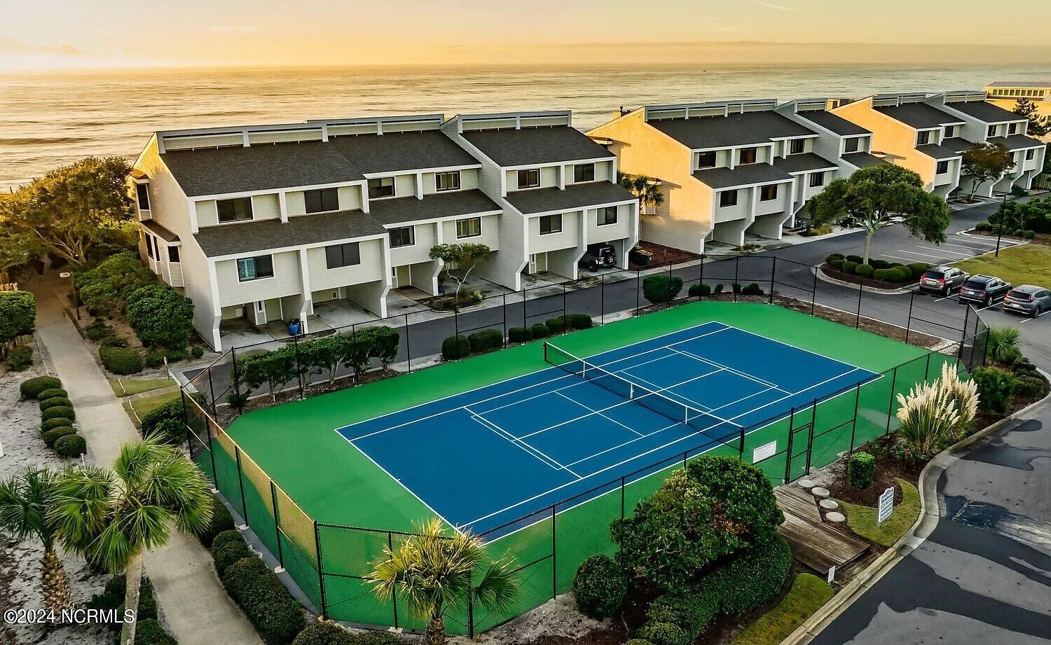 A tennis court surrounded by modern buildings with a view of the ocean.