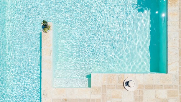 Vue aérienne d’une piscine rectangulaire à l’eau turquoise et limpide, entourée d’une terrasse carrelée.