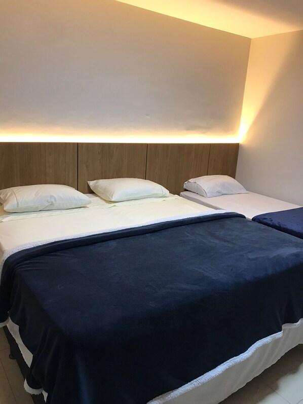 A hotel room with two beds, each with white bedding and a dark blue blanket. The room has a wooden headboard and a wall-mounted light fixture.
