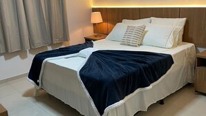 Ett modernt hotellrum med en stor säng, ett nattduksbord, en lampa och utsikt över staden genom fönstret.