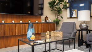 A modern living room with a flat-screen TV, a glass coffee table, a grey armchair, a small side table, and a large potted plant. - Luxury condo with pool, jacuzzi and private terrace (Cabo San Lucas)