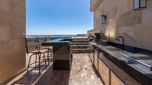 An outdoor kitchen with a view of the beach, stone walls, and a pergola. - Luxury condo with pool, jacuzzi and private terrace (Cabo San Lucas)