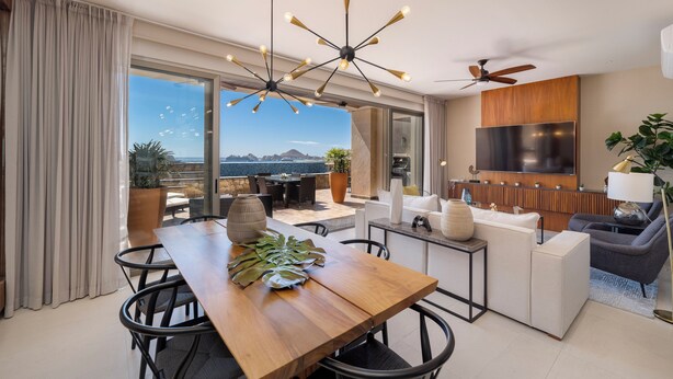 A modern living room with a dining area, large windows, a TV, and a ceiling fan. - Luxury condo with pool, jacuzzi and private terrace (Cabo San Lucas)