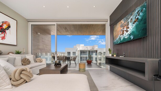 A modern living room with a large window, a sofa, a coffee table, and a flat-screen TV mounted on the wall. - Stunning Penthouse with Private Terrace & Jacuzzi Views (Cabo San Lucas)
