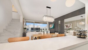 A modern kitchen with a marble countertop, wooden chairs, and pendant lighting. - Stunning Penthouse with Private Terrace & Jacuzzi Views (Cabo San Lucas)