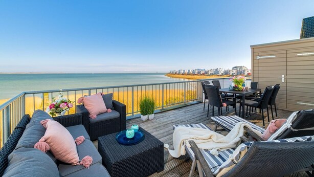 A deck with outdoor furniture, a table, and a view of the sea and buildings. - Stunning apartment in Olpenitz (Olpenitz)