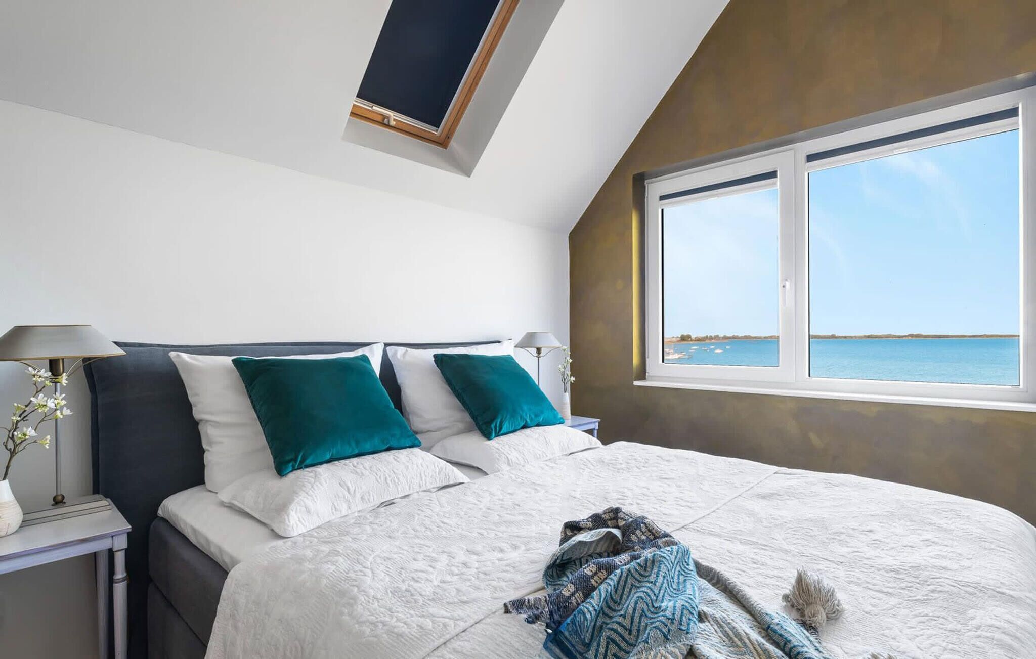Ein Schlafzimmer mit einem großen Bett, zwei Nachttischen, einem Oberlicht und einem Fenster mit Meerblick.