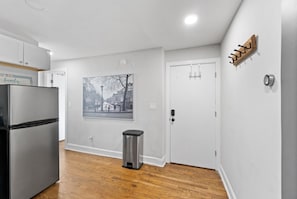 Compact kitchen with a refrigerator, trash bin, and coat rack, offering a convenient space for preparing meals.