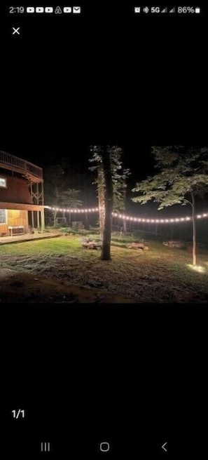 A nighttime view of a building with a balcony, surrounded by trees and string lights.