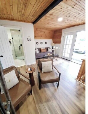 A cozy living room with a wooden ceiling, a sofa, a coffee table, and a glass door leading outside.