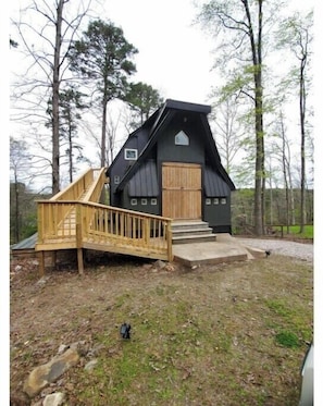 A cabin with a wooden deck and a steep staircase leading to a wooden door.