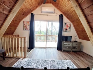 A high-ceilinged room with wooden beams, a large window, and a balcony.