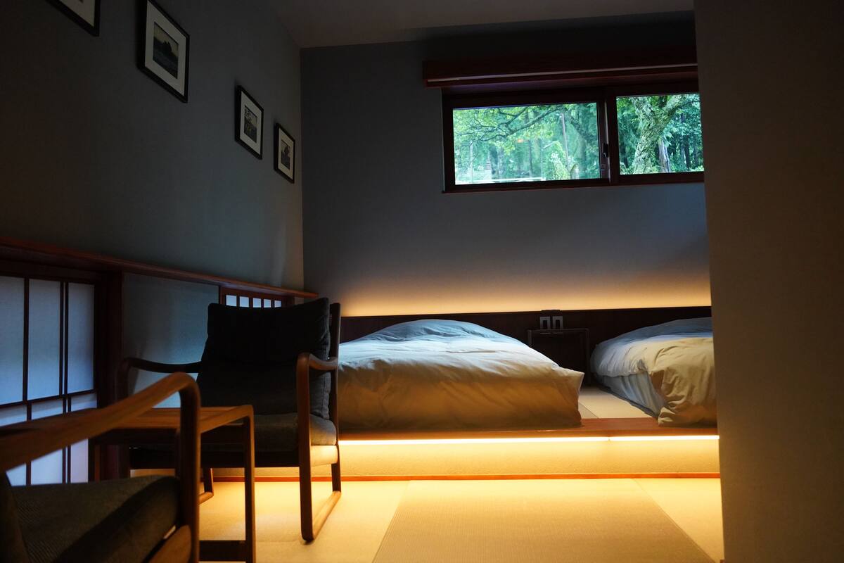 A bedroom with a bed, a chair, a window, and framed pictures on the wall.