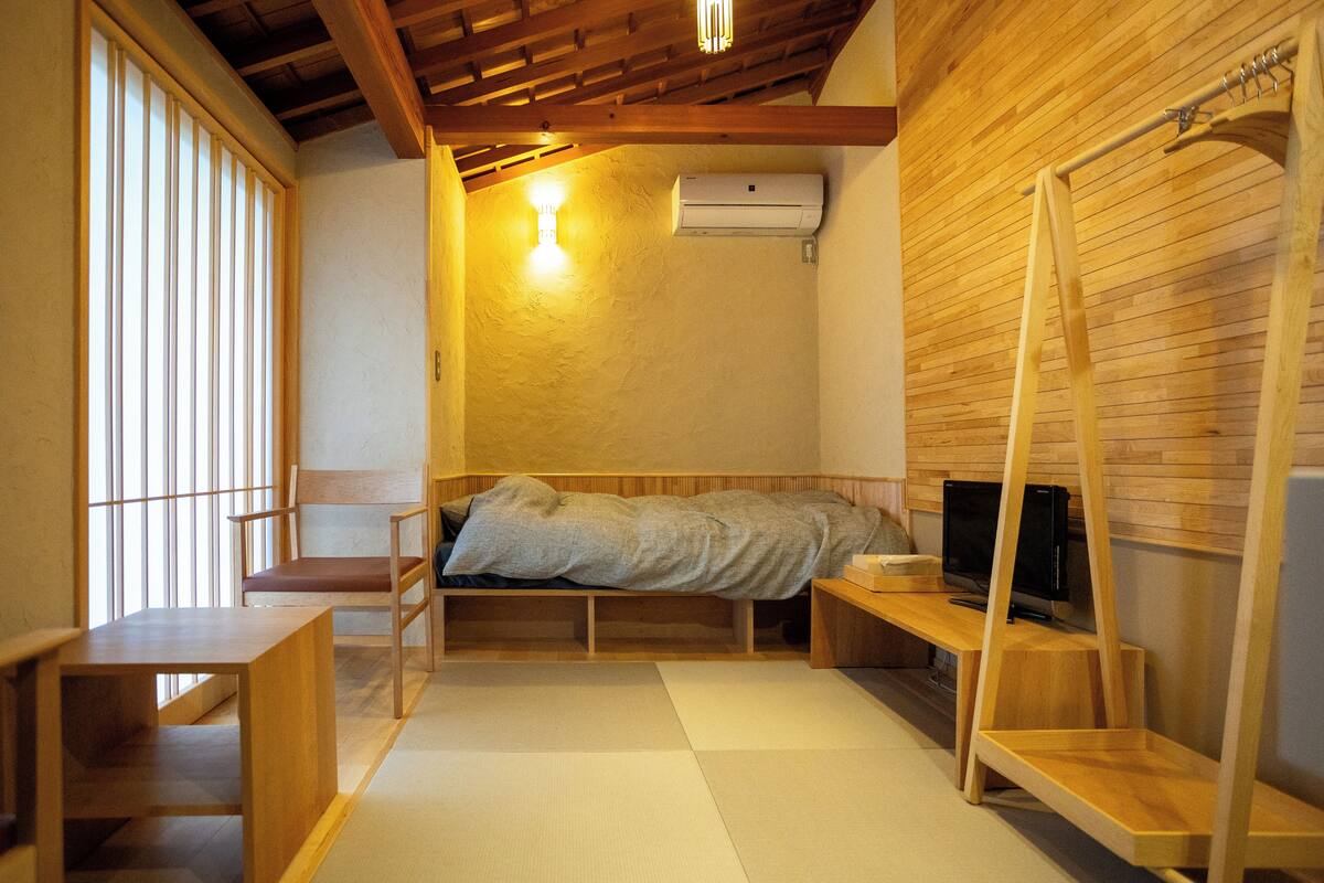 A compact room with a bed, a TV, a wooden desk, and a chair.