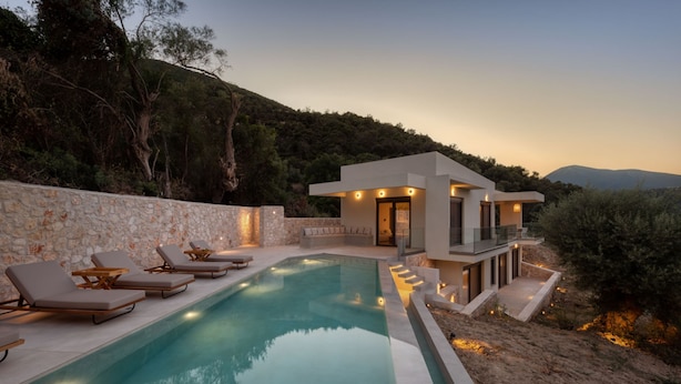 A modern poolside area with lounge chairs, a stone wall, and a building with a balcony. - Villa Eptanisa in Sivota (Lefkada)