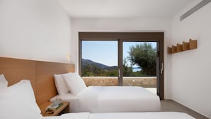 A modern hotel room with two beds, a wooden headboard, a nightstand, and a large sliding glass door leading to a balcony with a scenic view. - Villa Eptanisa in Sivota (Lefkada)