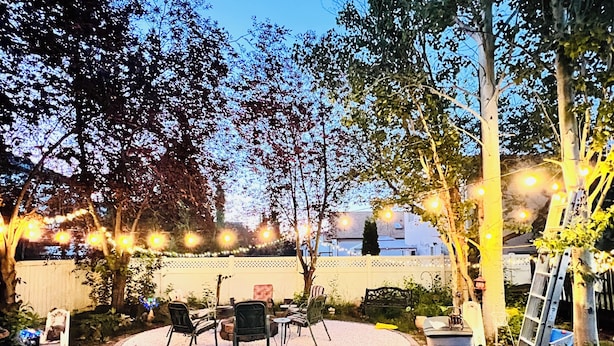 An outdoor patio area with a circular seating arrangement, surrounded by trees and a white fence.