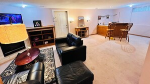 A living room with a TV, leather sofa, and a dining area with wooden chairs.